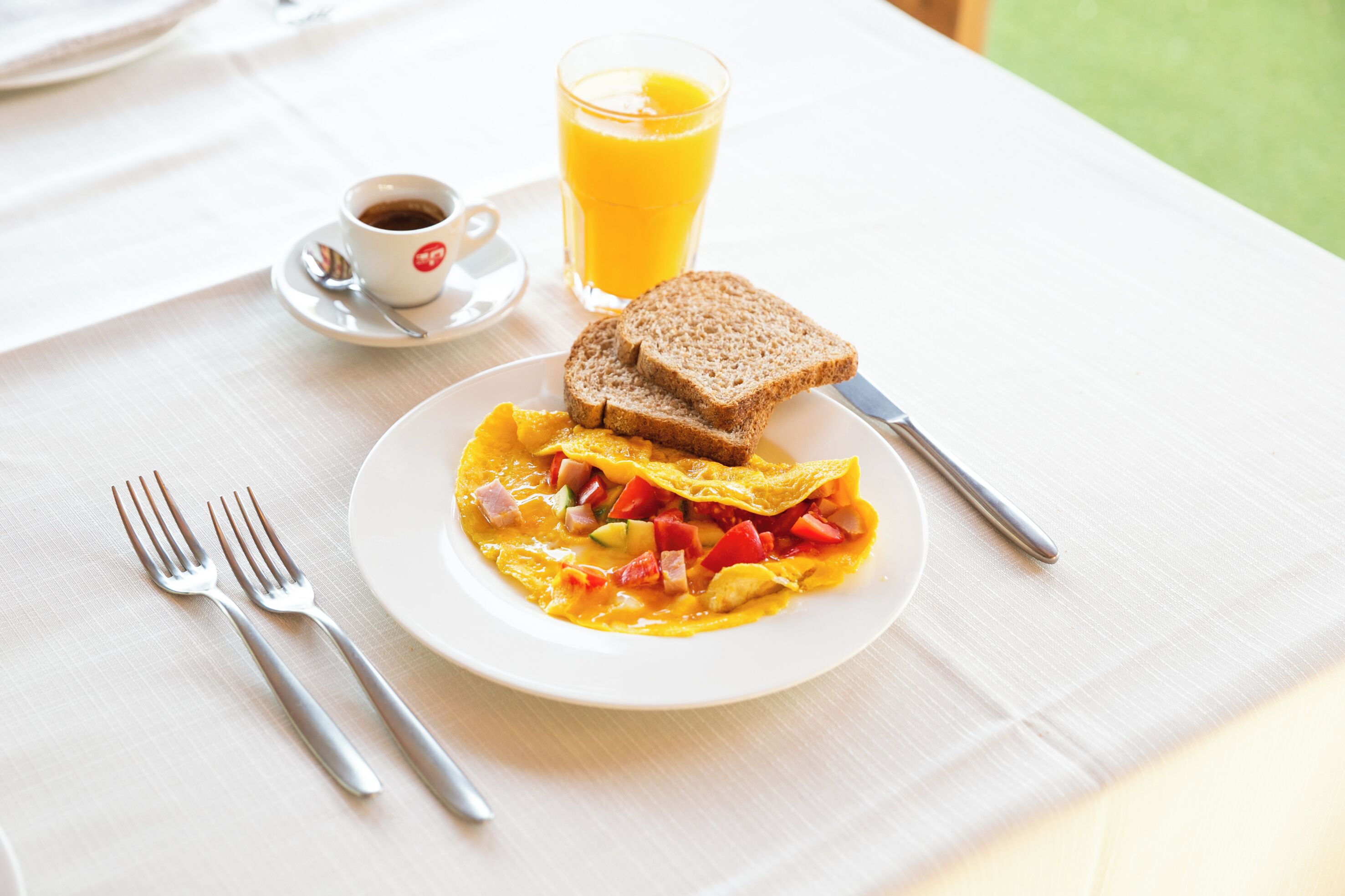 Un desayuno con una fuente de huevos revueltos, tostadas y un vaso de zumo de naranja sobre una mesa.