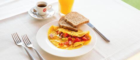 Un desayuno con una fuente de huevos revueltos, tostadas y un vaso de zumo de naranja sobre una mesa.