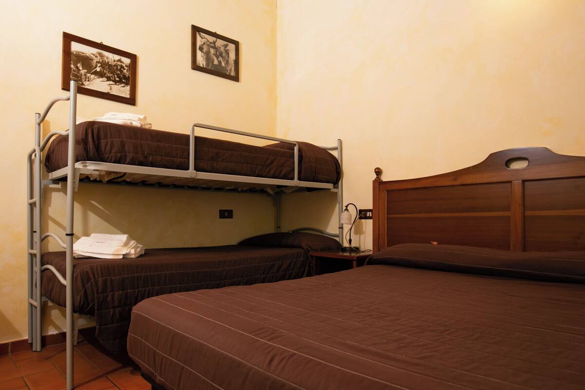 A dormitory room with bunk beds, a wooden headboard, and two framed pictures on the wall.