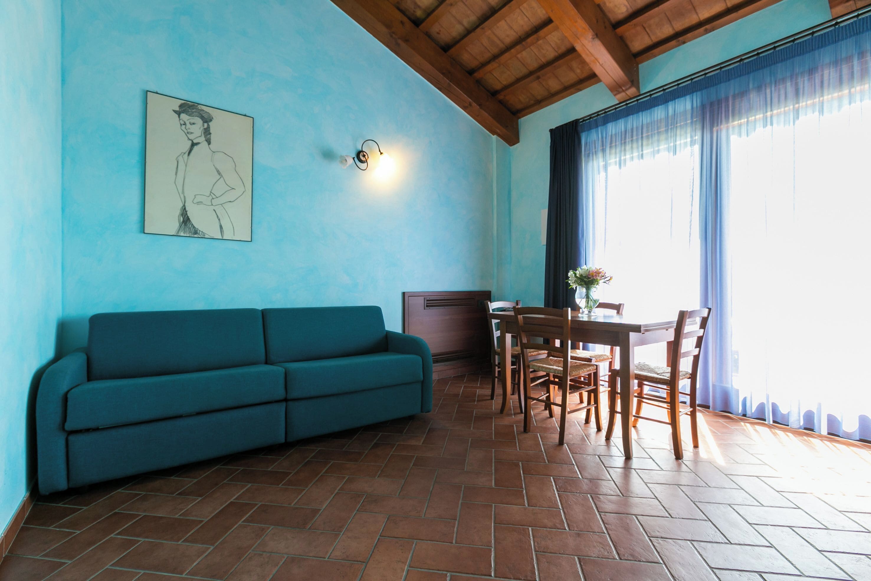 Une pièce avec un canapé bleu, une table à manger en bois, des chaises et un luminaire fixé au mur.