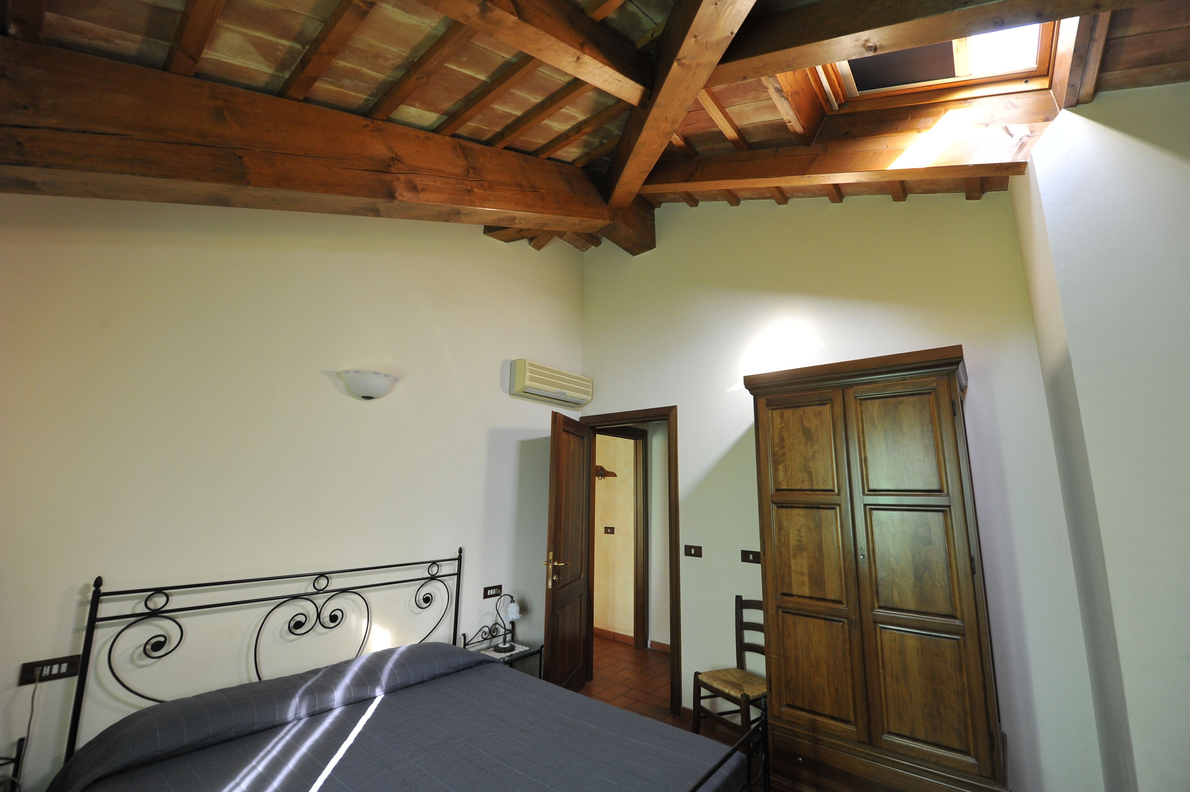 Une chambre à coucher comprenant un lit, une armoire en bois, une chaise, une table de chevet et une lucarne.