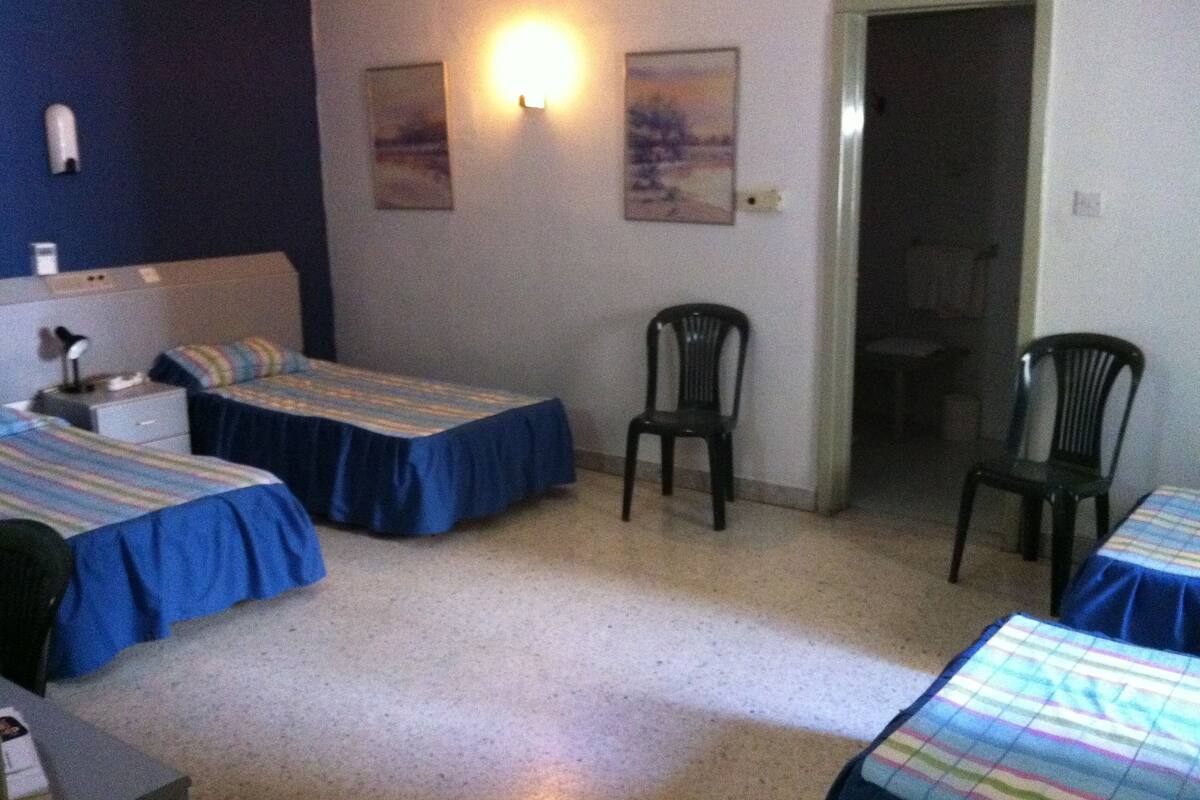 A room with two single beds, a chair, a desk, and a nightstand.