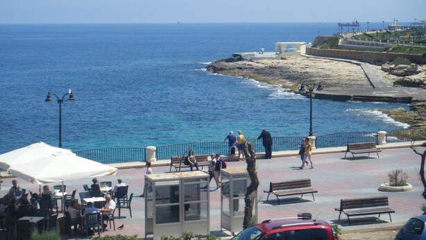 A coastal promenade with outdoor seating, a rocky shoreline, and a view of the sea. - Hotel Roma (Sliema)