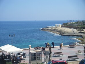A coastal promenade with outdoor seating, a rocky shoreline, and a view of the sea. - Hotel Roma (Sliema)