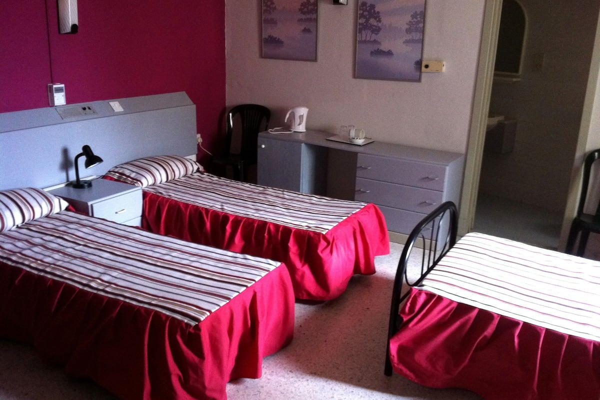 A hotel room with two beds, a desk, a chair, a nightstand, a lamp, and a painting on the wall.