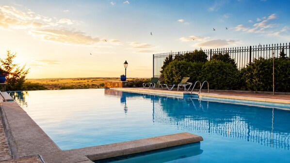 A swimming pool with a view of the sunset, a lamp post, and a fence.