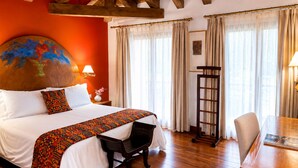 Habitación de hotel con una cama grande, un escritorio y una silla. El techo es de madera y hay un cuadro en la pared.