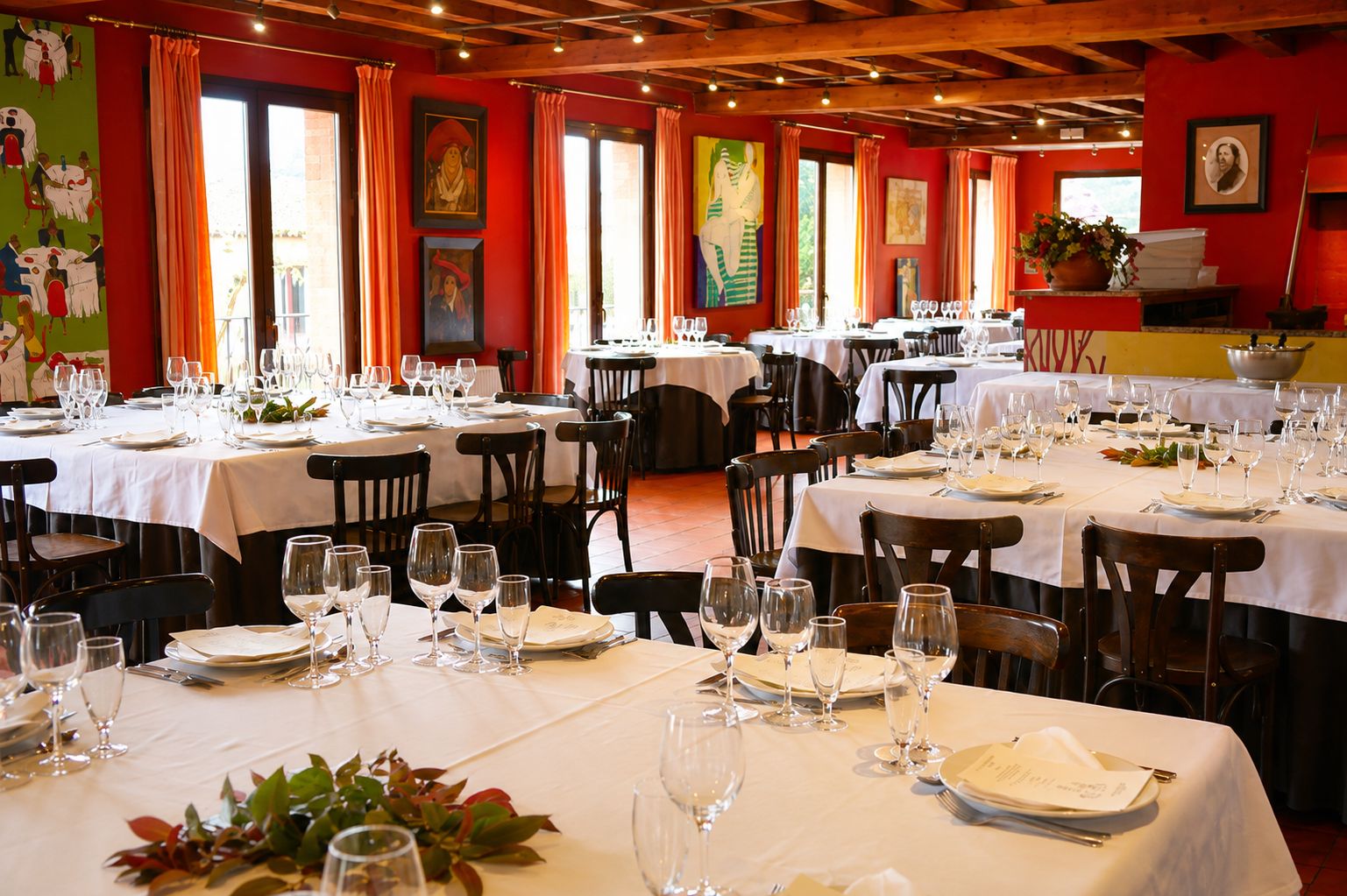 Un restaurante con varias mesas dispuestas para comer, con una pared roja decorada con obras de arte y un techo de madera.