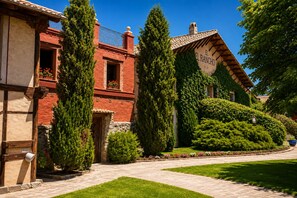 Un edificio tradicional con un letrero que dice 'EL RANCHO' y un jardín bien cuidado con setos y un camino pavimentado.