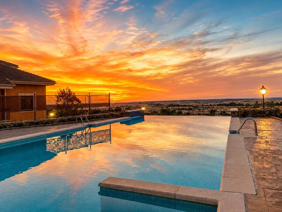 A swimming pool with a sunset view, a covered patio area, and a street lamp.