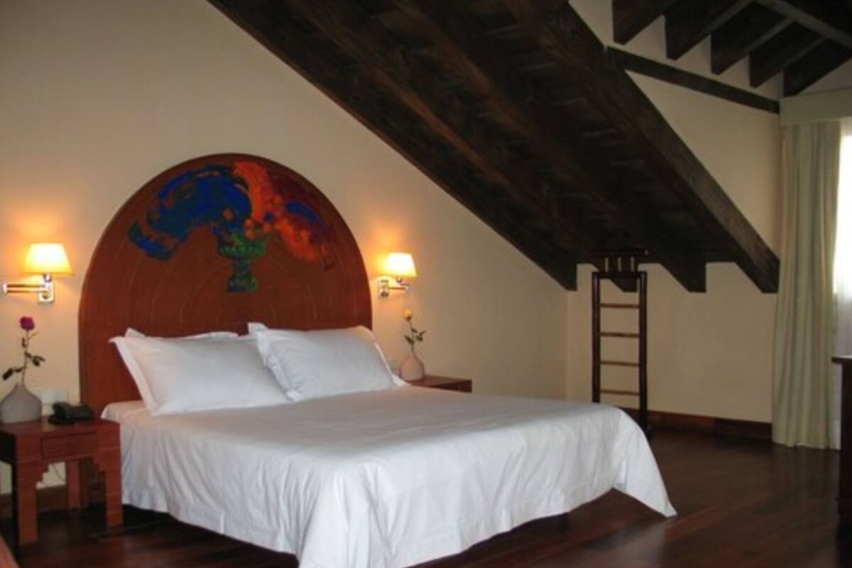 Une chambre à coucher avec un grand lit, une tête de lit en bois, deux lampes de chevet et une échelle en bois.