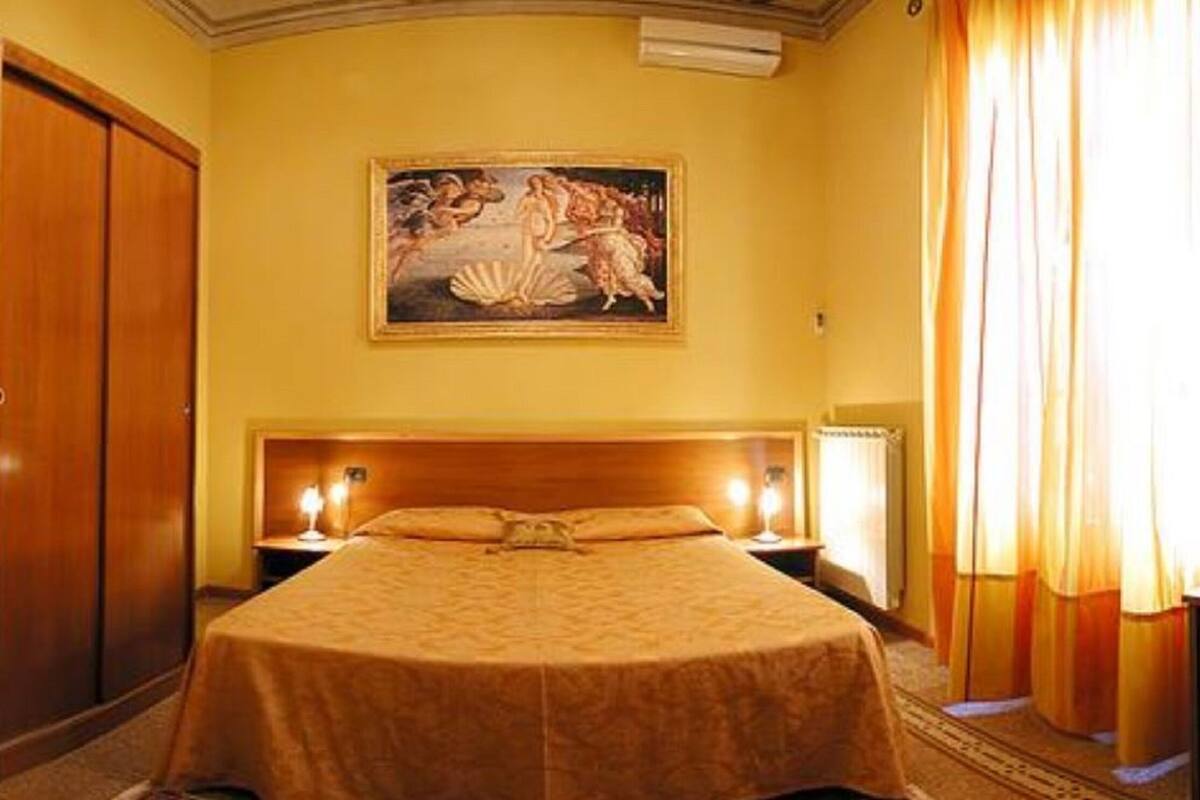 A hotel room with a large bed, a wooden wardrobe, a painting on the wall, and a window with curtains.