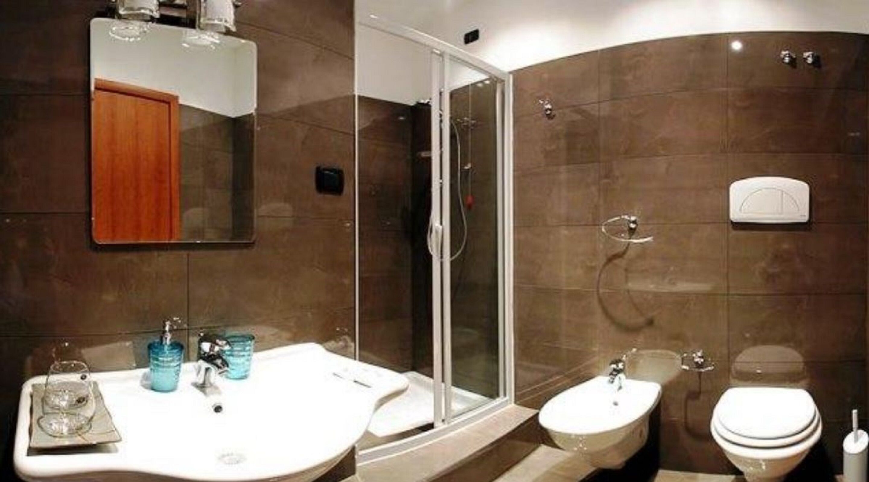 A modern bathroom with a glass-enclosed shower, a white sink with a mirror above it, and a bidet.