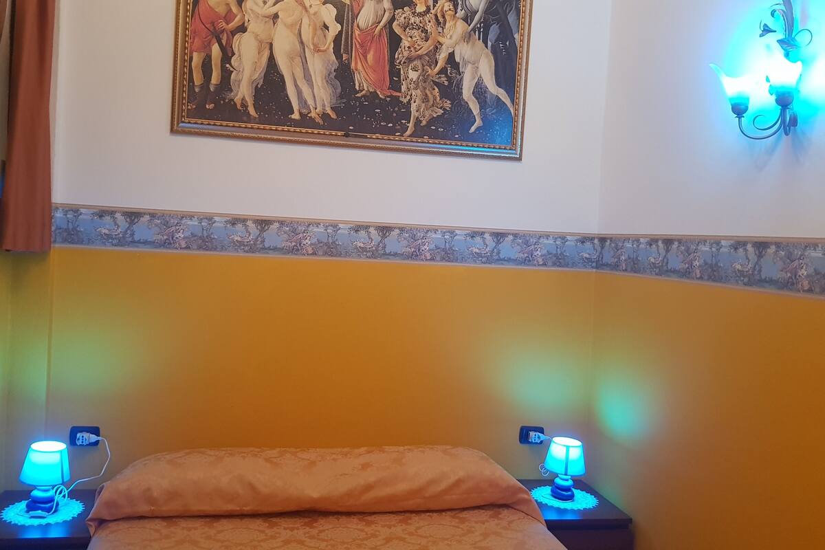 A bedroom with a bed, two bedside lamps, a painting on the wall, and a patterned wall border.
