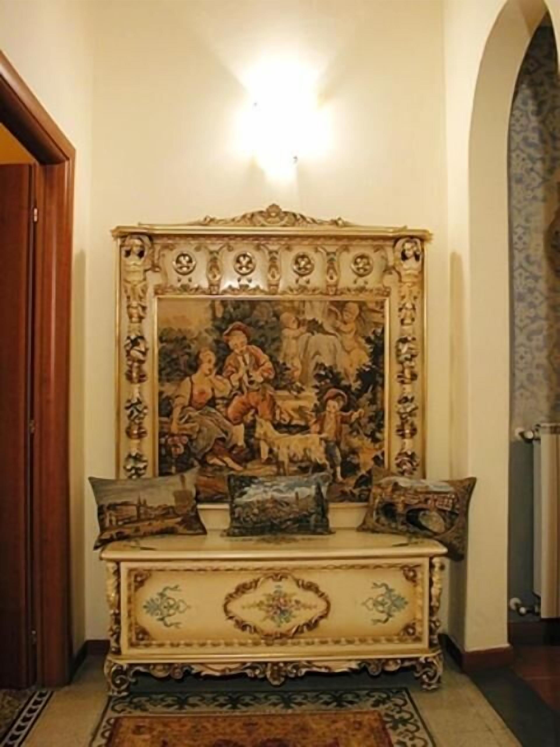 Una habitación con un cuadro grande y ornamentado en la pared, una puerta de madera y un tapete estampado en el suelo.