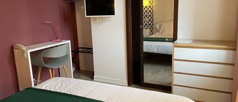 A hotel room with a bed, a desk with a chair, a TV, a wardrobe, and a mirror.