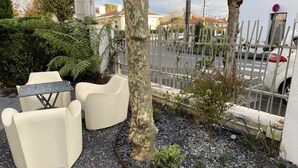 Zona de pati amb mobiliari exterior, un arbre i un camí de grava.