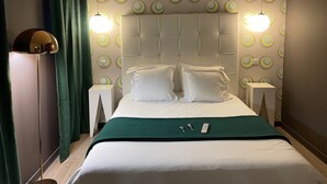 Habitació d'hotel amb llit, dues taules de nit, una làmpada de peu i un mur amb dibuixos circulars.