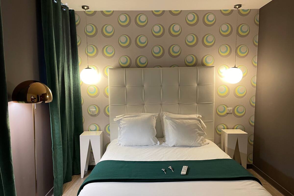 A hotel room with a bed, two bedside tables, a floor lamp, and a wall with circular patterns.