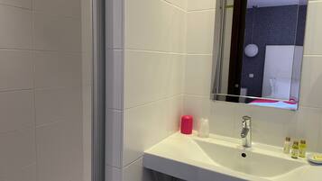Een badkamer met witte tegels, een wastafel met spiegel en toiletartikelen op het aanrecht.