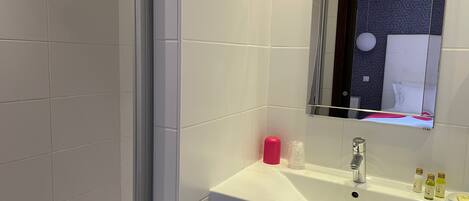 A bathroom with white tiles, a sink with a mirror, and toiletries on the counter.