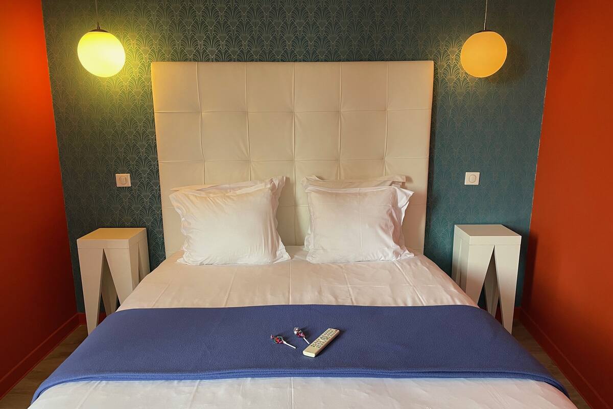 A hotel room with a large bed, two white pillows, a blue blanket, and two bedside tables with lamps.