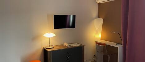 Habitación de hotel con cama, escritorio con lámpara, teléfono, televisor de pantalla plana en la pared y equipo de aire acondicionado.