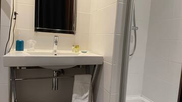 A bathroom with a white sink, mirror, and shower. There are towels and toiletries on the sink.