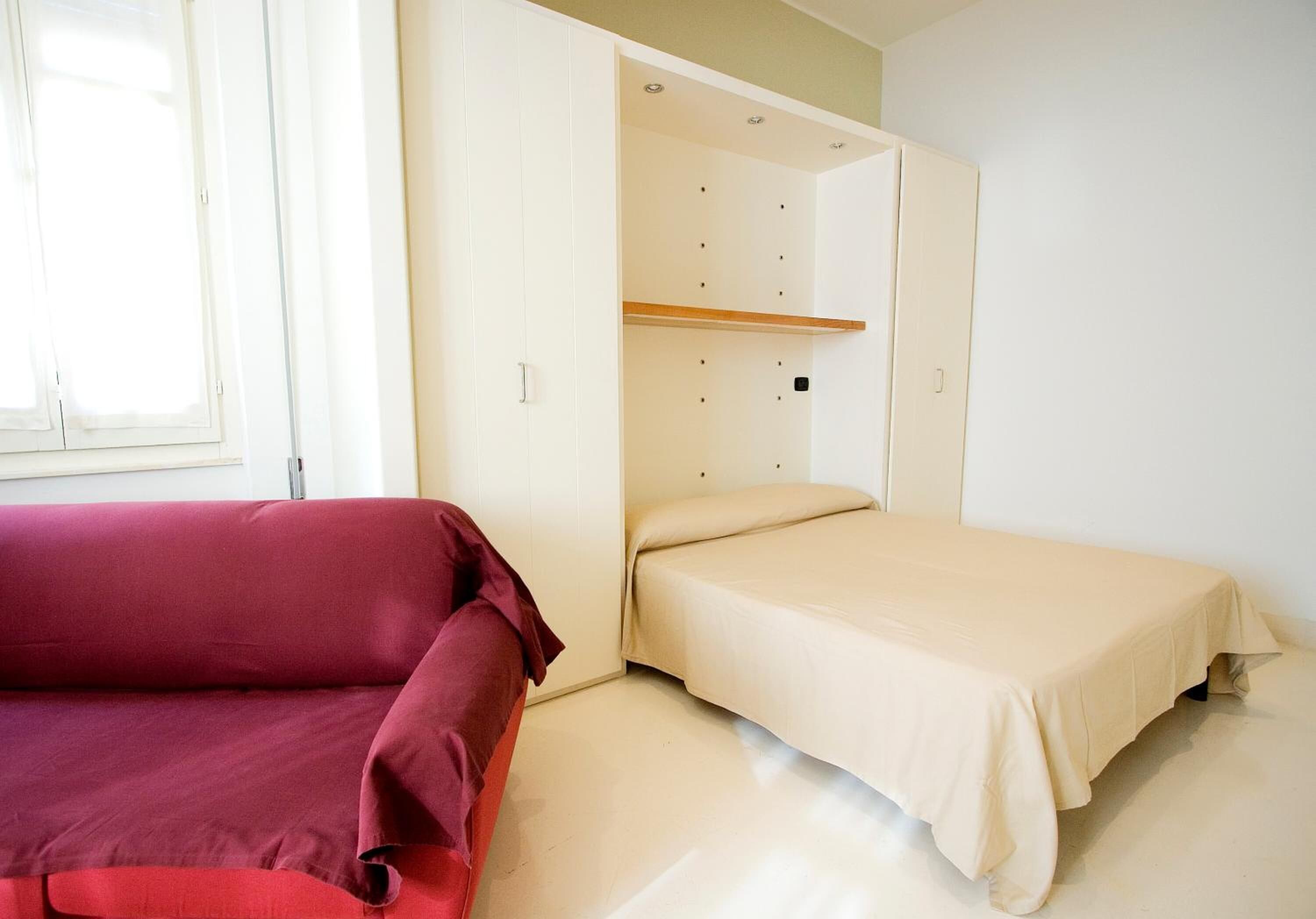 A room with a bed, a red sofa, and a wardrobe with a mirror.
