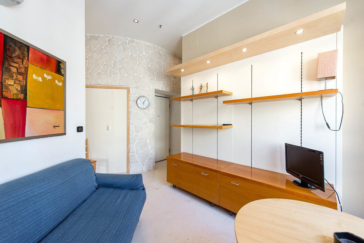 A modern living room with a blue sofa, a wooden entertainment unit with shelves, a flat-screen TV, and a stone accent wall.