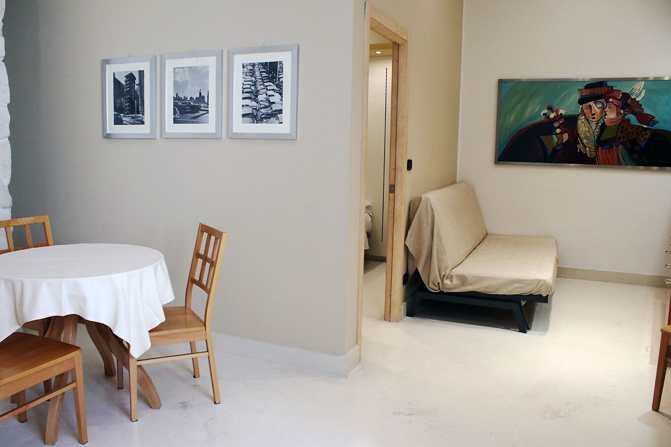 Een kamer met een ronde tafel, twee stoelen, een bank en drie ingekaderde foto’s aan de muur.