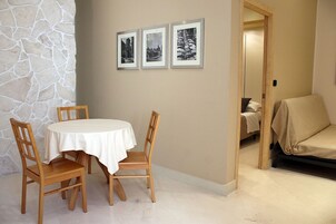 Un comedor con una mesa redonda y cuatro sillas de madera, una pared de piedra y tres cuadros enmarcados.