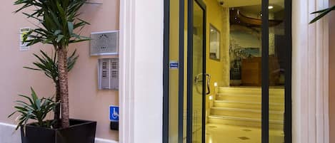 Entrada de un hotel con puerta de vidrio, una planta en maceta y un letrero que indica acceso para personas con discapacidad.