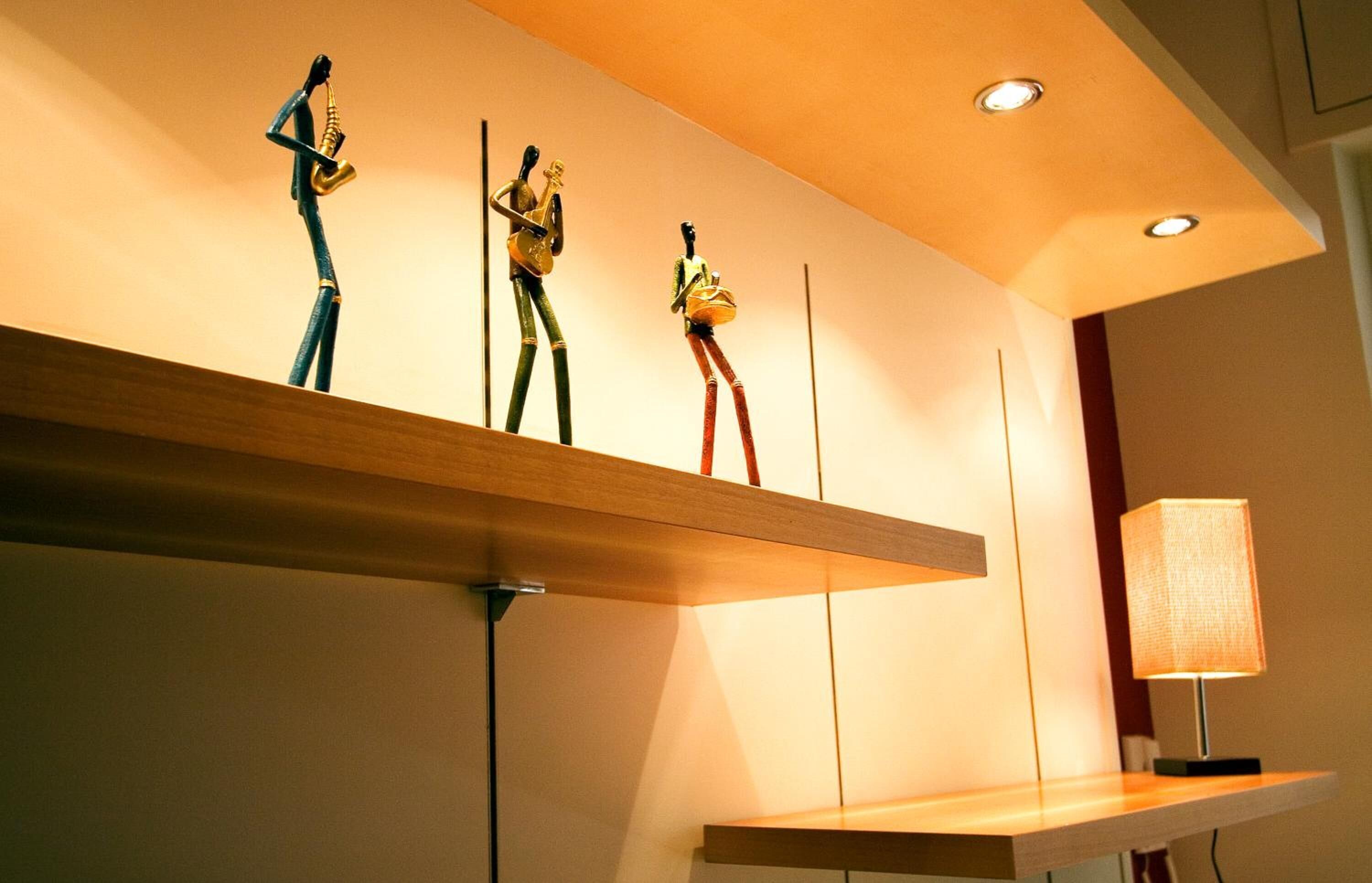 Un intérieur moderne avec une étagère en bois où sont exposées trois sculptures, une lampe et des spots encastrés au plafond.