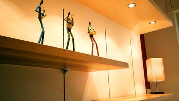 Un intérieur moderne avec une étagère en bois où sont exposées trois sculptures, une lampe et des spots encastrés au plafond.