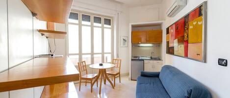 A modern kitchen with wooden cabinets, a dining area with a round table and chairs, and a blue sofa.