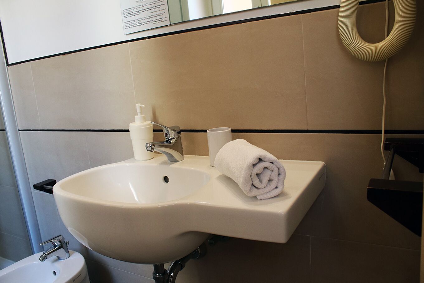 Ein Badezimmer mit einem weißen Waschbecken, einem Handtuch, einer Seifenspender und einer Tasse.