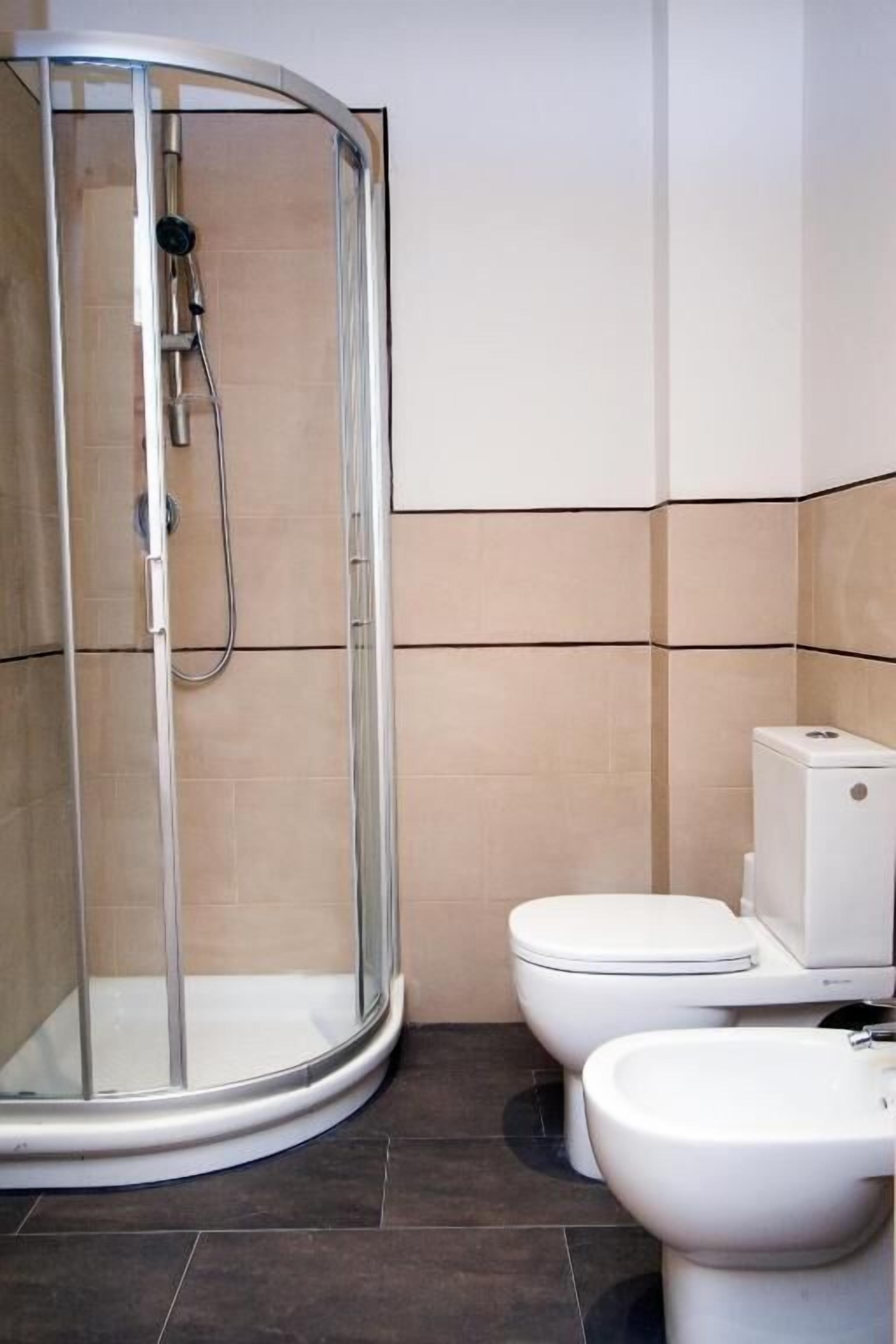 Un baño con ducha de vidrio, dos inodoros y un bidé.