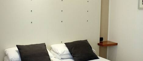 Una cama bien hecha con una colcha color beige y dos almohadas, una negra y una blanca, en una habitación de diseño moderno y sencillo.