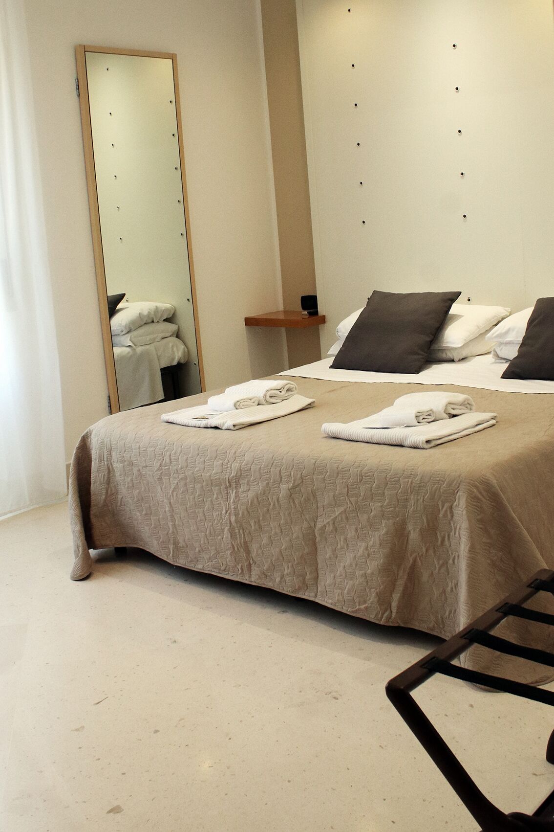 A modern hotel room with a large bed, a bedside table, a mirror, and a wall-mounted shelf.