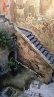 A staircase with stone steps leading up to a door, surrounded by a weathered wall and some greenery.