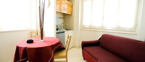 A compact living space with a dining table, a red sofa, and a kitchen area.