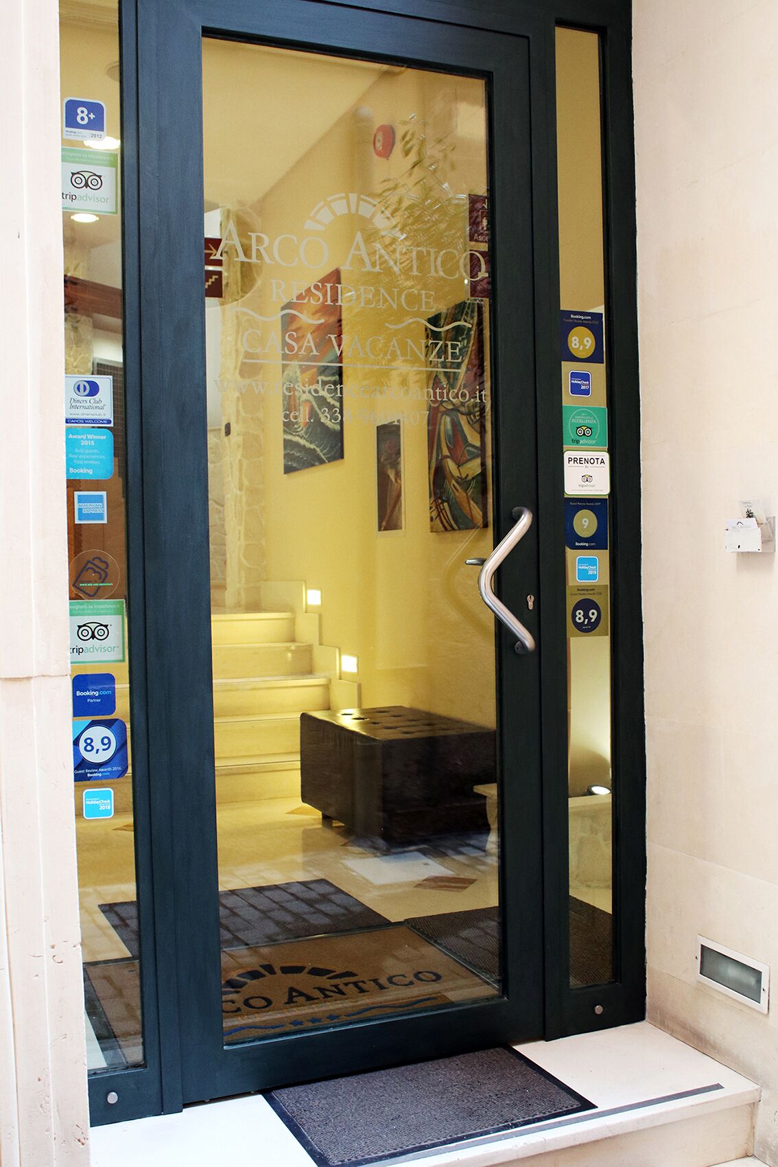 L’entrée d’un hôtel, avec une porte en verre, un comptoir d’accueil et divers panneaux, dont un logo TripAdvisor.