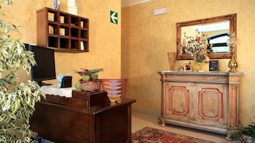 Una habitación con un escritorio de madera, televisión, estante con cajas, espejo y alfombra estampada.