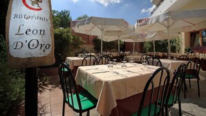 An outdoor dining area with tables and chairs, a sign for Ristorante Leon D'Oro, and umbrellas. - Leon d'Oro (Corleone)