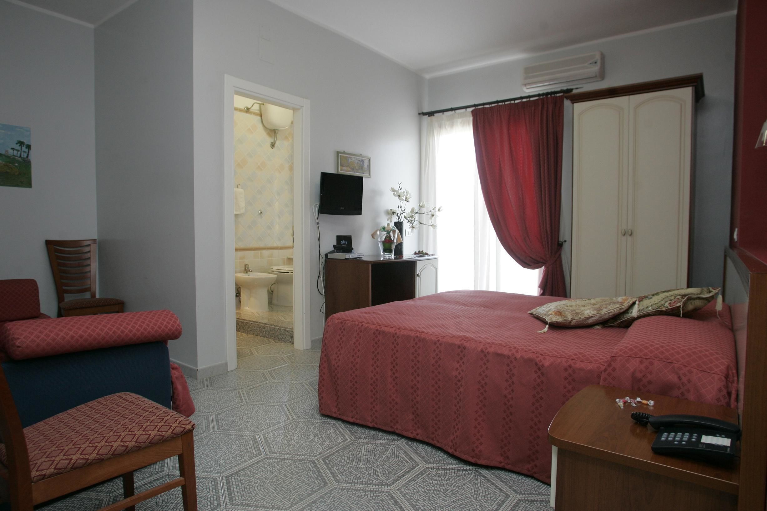 A hotel room with a bed, a desk with a telephone, a chair, a television, and a bathroom visible through an open door.