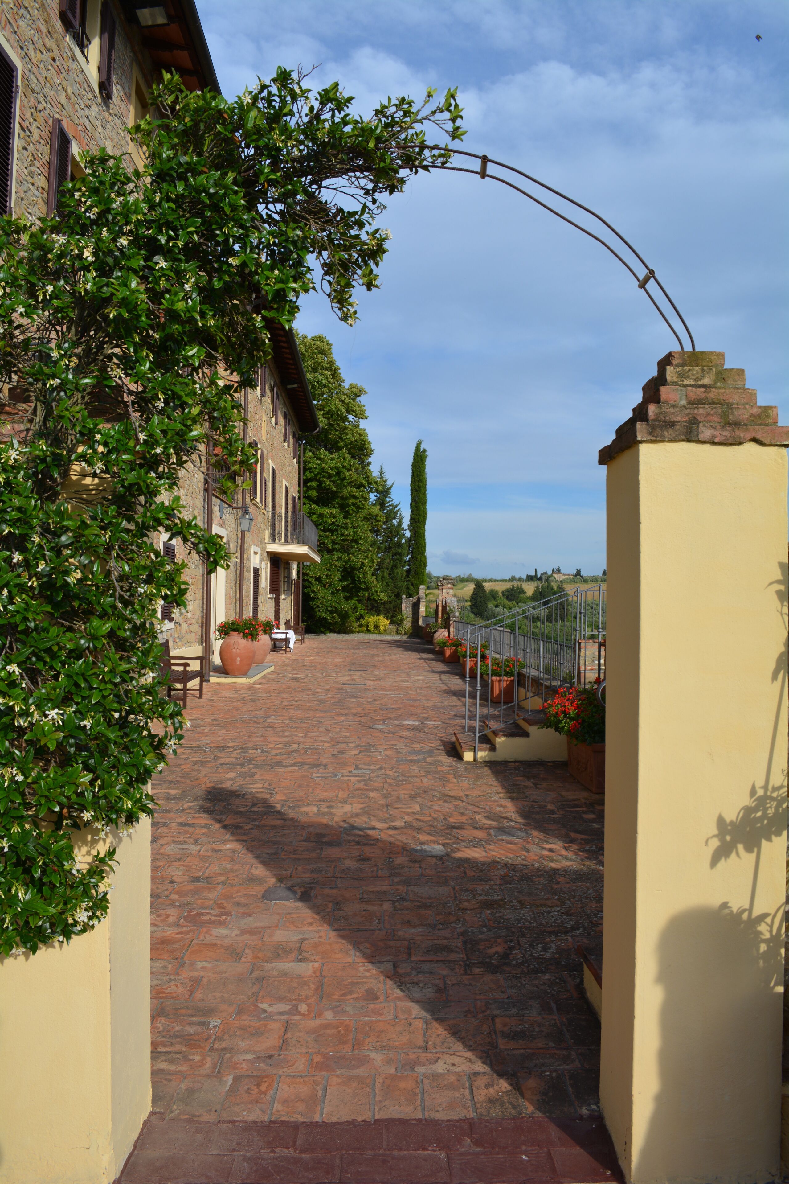 A paved pathway leading to a building with a yellow wall and a metal archway.