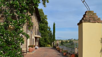 A paved pathway leading to a building with a yellow wall and a metal archway.
