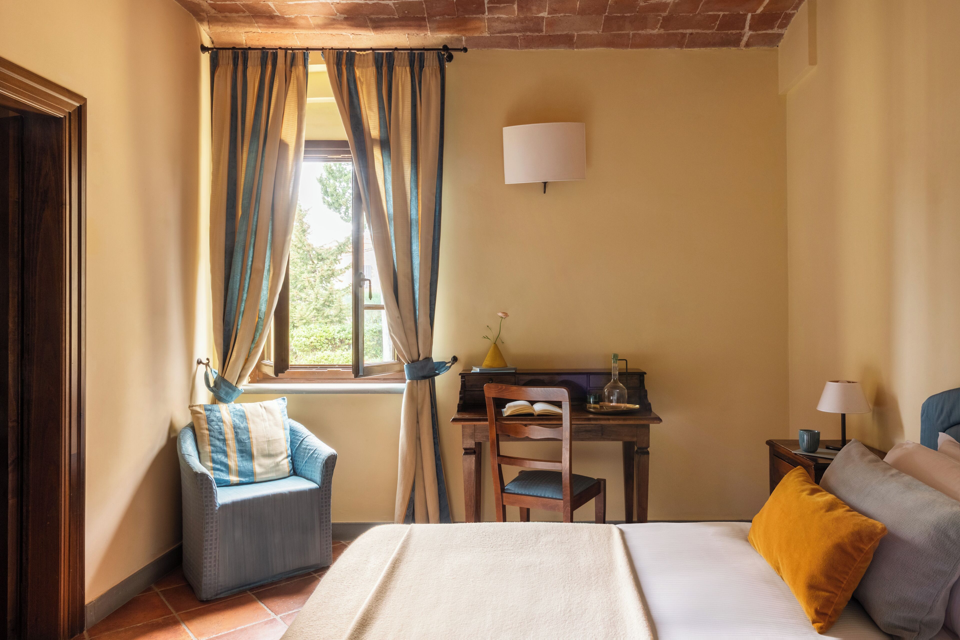 A bedroom with a bed, a desk, a chair, and a window with curtains.