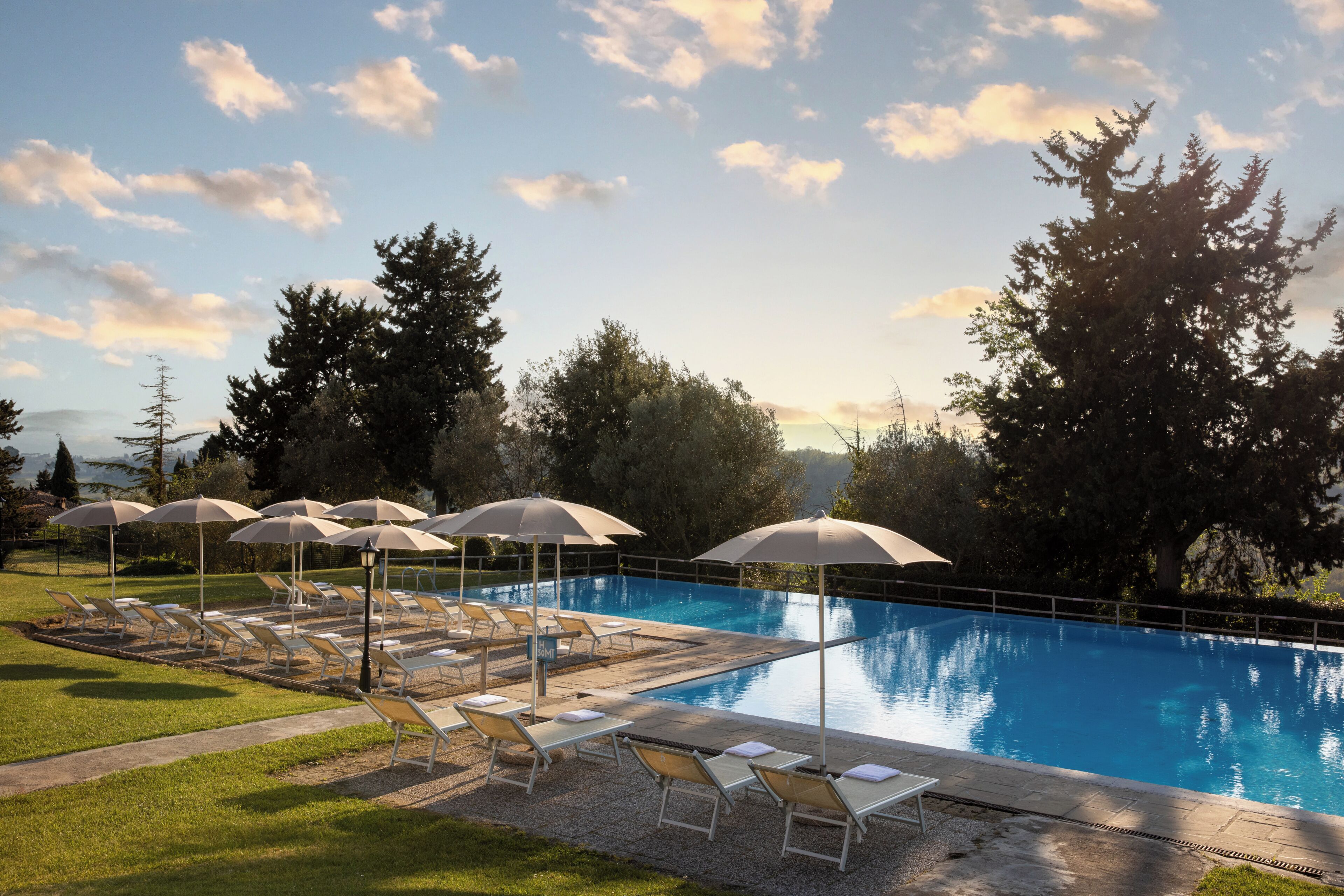 A swimming pool with lounge chairs and umbrellas, surrounded by trees and a clear sky.
